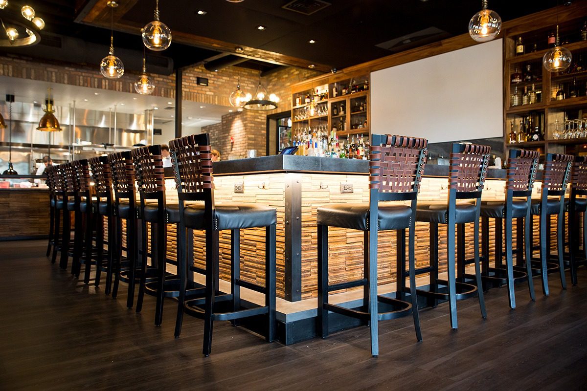 Modern bar with wooden stools and warm lighting.