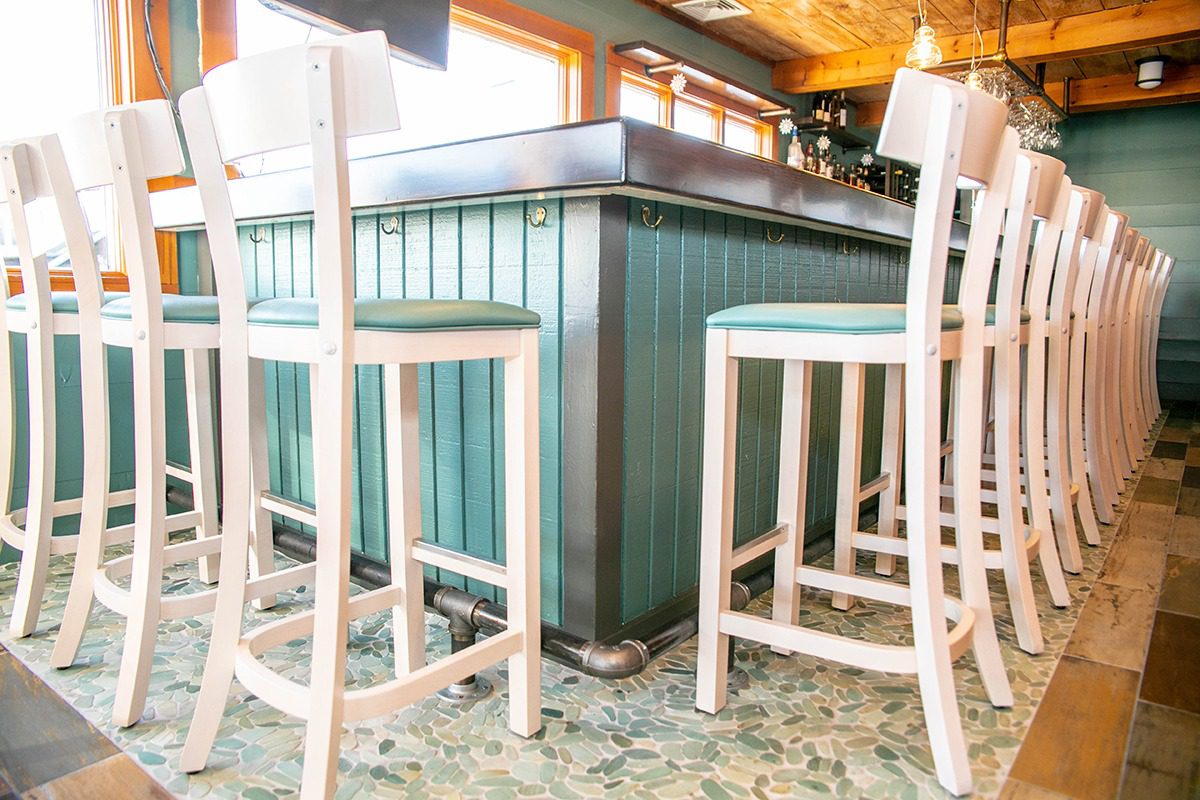 White wooden bar stools around a green bar counter in a bright room.