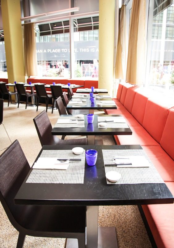 Modern restaurant tables set with blue glasses and menus.