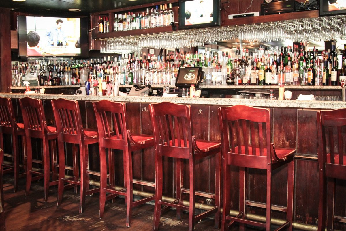A row of red wooden bar stools at a well-stocked bar counter.