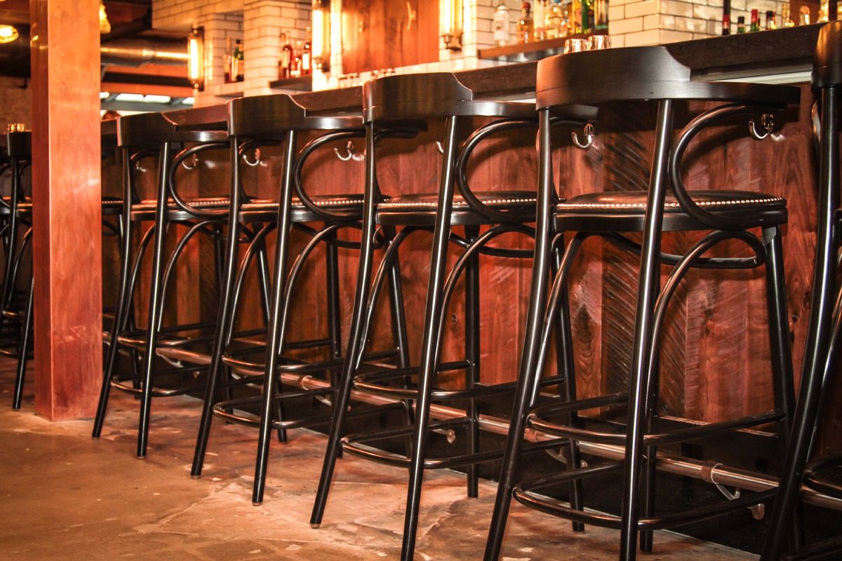 A row of black bar stools lined up at a wooden bar counter.