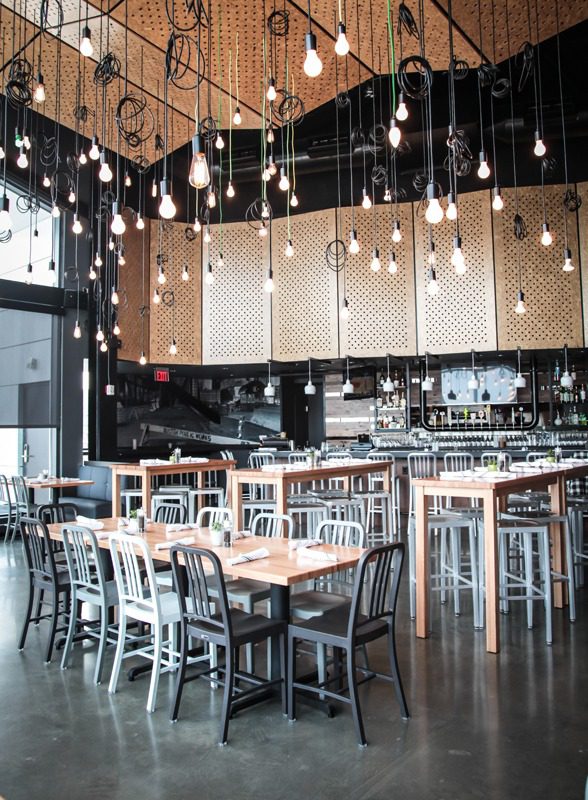 Modern restaurant interior with hanging light bulbs and wooden tables.