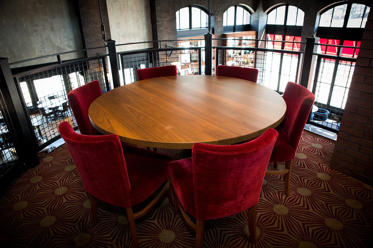 Round wooden table surrounded by six red velvet chairs in a cozy room.