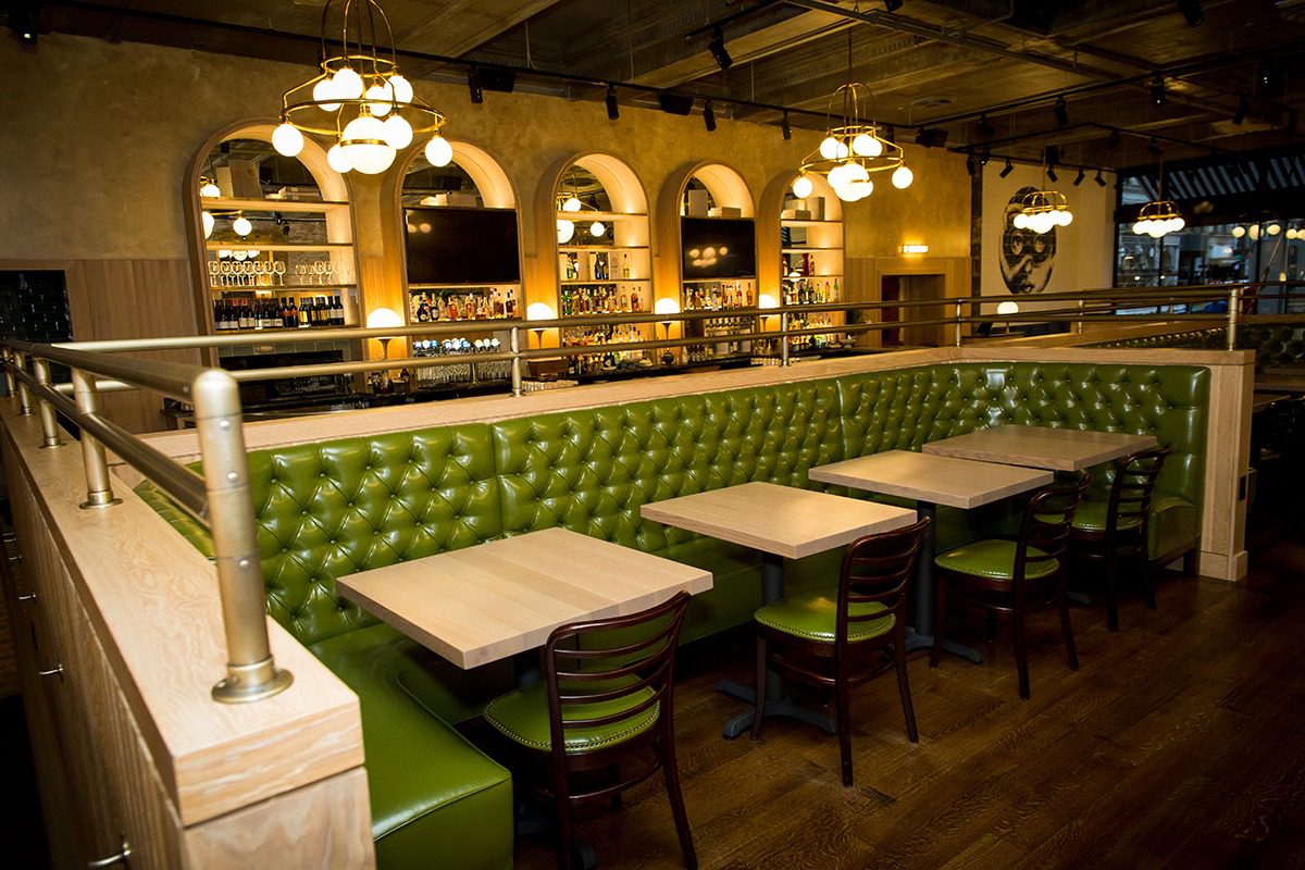 Cozy restaurant interior with green leather seating and warm lighting.